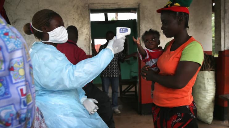 A health worker in protective gear checks a woman's temperature